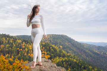 A beautiful young woman in white leggings poses on top of a mountain. Outdoor health and sports....