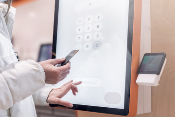 A user engages with a digital kiosk that facilitates seamless and contactless payment processing for transactions. The woman pays through the payment terminal with a credit card. The touch screen