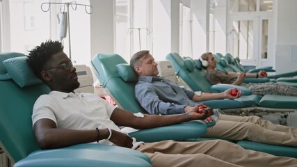 Three male donors reclining in chairs using stress balls in clean, well-lit blood donation center - Powered by Adobe