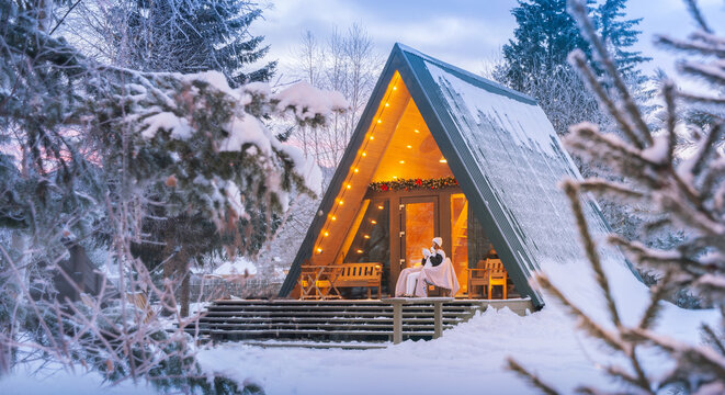 A woman drinks hot chocolate or coffee in winter in a house near the forest on Christmas eve. Warm moments on a chilly winter morning at a cozy A-frame cabin in the forest with tea and tranquility - Powered by Adobe
