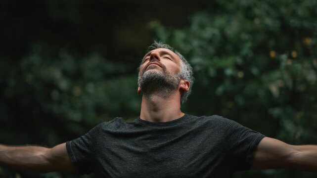 Embracing Serenity: A middle-aged man, arms outstretched, absorbs the tranquility of nature, his face lifted towards the sky. Capturing moments of reflection and spiritual connection.