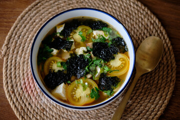 Spicy soup with yellow cherry tomatoes, crispy nori chips, cheese and cilantro. Top view, close-up, white plate, mushroom broth, chili pepper.