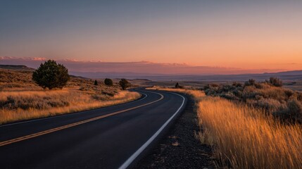 A winding road snakes through golden grasslands as the sun sets over distant hills, creating a tranquil atmosphere in the wide-open landscape. The sky is painted with soft hues of orange and purple.