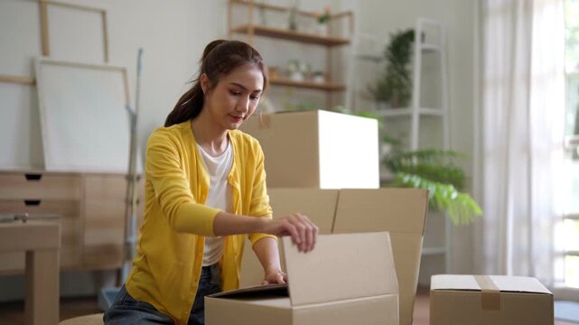 Asian woman carefully packing personal belongings into moving boxes preparing new home apartment relocation