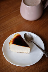 Side view of delicious slice of basque cheesecake on white plate. Cappuccino, chair, wooden table