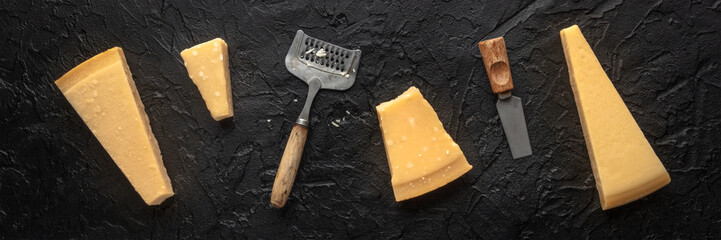 Parmesan cheese wedges on a black background, overhead flat lay shot with a cheese grater and a knife, panorama