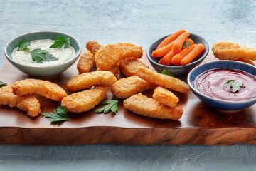 Chicken nuggets with fresh vegetables and dips, on a wooden board. Tasty dinner, a close-up