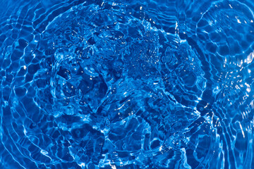 Blue water with ripples on the surface. Defocus blurred transparent blue colored clear calm water surface texture with splashes and bubbles. Water waves with shining pattern texture background.
