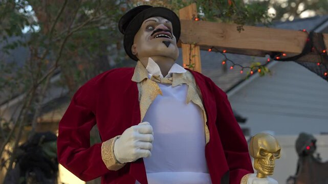 Close-up Halloween decoration of a ringmaster in a red coat holding a gold skull cane. Outdoor suburban yard scene with orange lights and a spooky holiday theme.