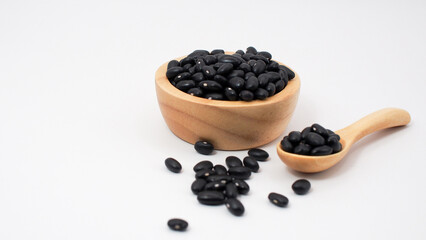 Raw black beans in a wooden bowl and spoon with some beans scattered on white background. Perfect for illustrating organic legumes