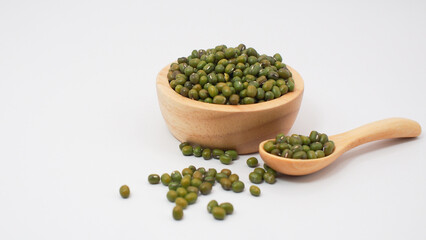 Raw mung beans in a wooden bowl and spoon with some beans scattered on white background. Perfect for illustrating organic legumes