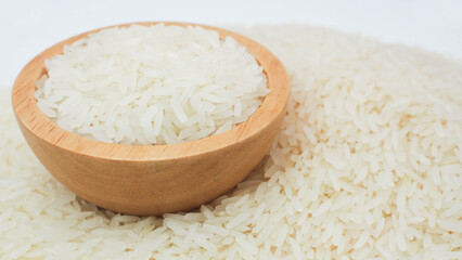 Raw white rice grains in a wooden bowl placed on a pile of rice with white background. Perfect for illustrating Asian food