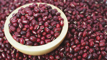 Closeup of raw red adzuki beans in a wooden bowl placed on a pile of beans background. Perfect for...