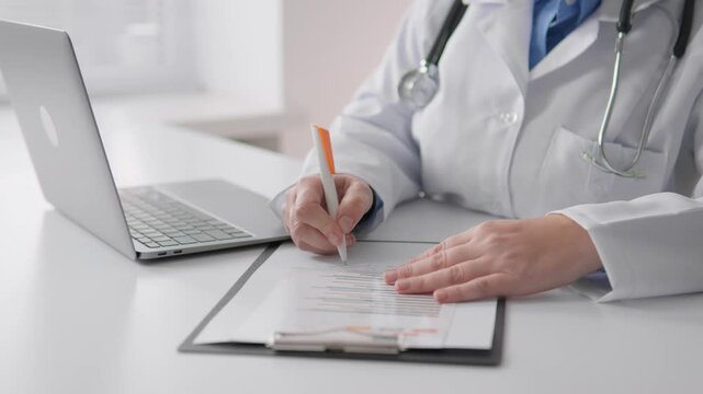 A healthcare professional in a lab coat is completing patient documentation on a clipboard while using a laptop for digital records, showcasing the blend of traditional and modern medicine.