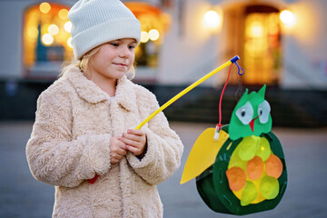 Little preschool kid girl holding selfmade traditional owl lanterns with candle for St. Martin procession. child happy about children and family parade in kindergarten. German tradition Martinsumzug