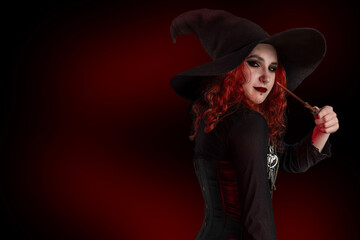 Witch with a magic wand casts a spell. Young woman, magician girl with red hair, dressed in...