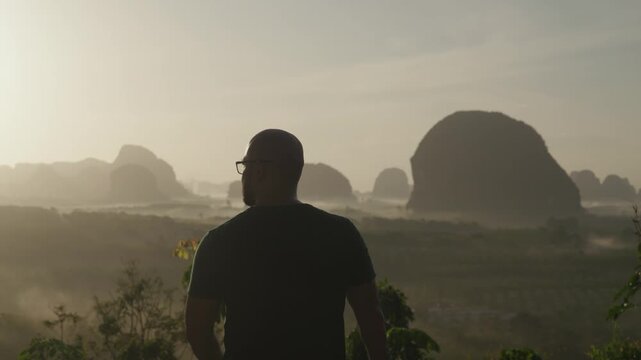 Silhouette of a man enjoying sunrise with misty mountain and forest view at Din Daeng Doi, Krabi, Thailand, creating a peaceful and scenic atmosphere.