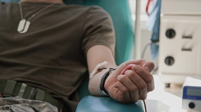 Close-up shot of arm of unrecognizable male soldier in military uniform gently squeezing stress ball for better blood flow during blood donation in clinic