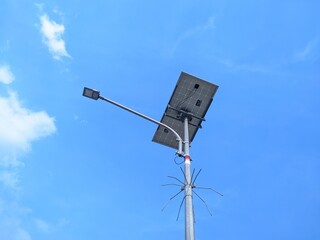 Solar-powered street light with a solar panel and LED lamp against a bright blue sky with scattered clouds.