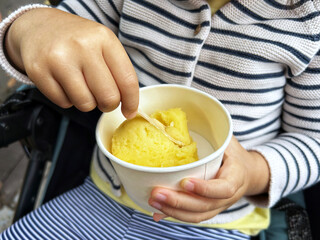 A child holding a plastic cup with ice cream outdoors, representing takeaway dessert and casual street food lifestyle.