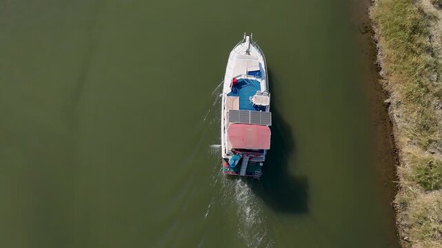 Aerial Top-Down View of a Double-Deck Passenger Ferry or Tour Boat Navigating Deep Green-Grey Water, capturing the stern and wake from a unique high angle.