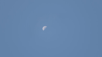 A crescent moon hangs in a bright blue sky as daylight persists in the late afternoon. The tranquil atmosphere invites reflection and appreciation of nature's beauty