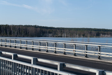 A bridge crosses a serene lake, reflecting the clear sky and bordered by lush greenery. The peaceful setting invites relaxation and contemplation