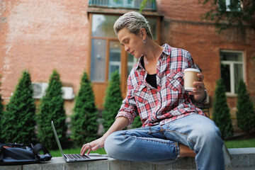 Obraz premium Stylish freelancer holding takeaway drink and using laptop outdoors 
