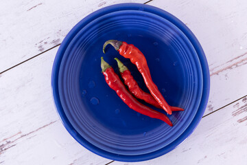 3 red hot chili peppers on a blue plate against a white-washed distressed wood surface.