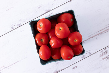 Pint of strawmato variety tomatoes, with water droplets, on white-washed distressed wood surface.