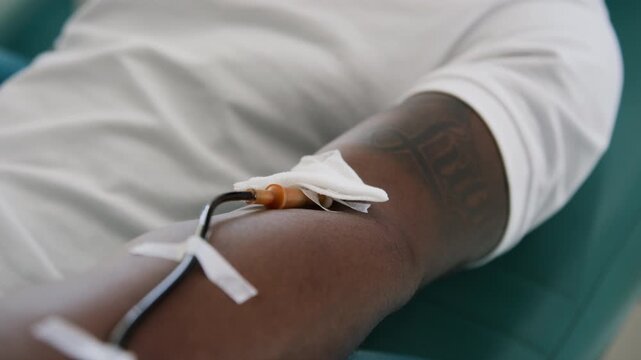 Close-up shot of arm of unrecognizable African American man with taped IV line and cotton ball near insertion site, donating blood in clinic