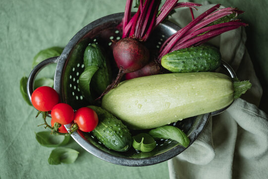 Close-up overhead view of beetroot, courgette, cherry tomatoes and cucumbers in a metal colander on a green tablecloth