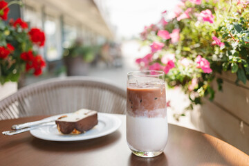 Close-up of an iced latte coffee and a slice of cake on a table at a street cafe in summer
