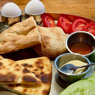 Close-up of a traditional Georgian breakfast with Georgian Imeruli khachapuri, soft boiled eggs, bread, tomato, cucumber, butter and honey