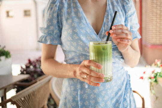 Close-up of a woman in a summer dress standing outdoors drinking an iced matcha latte