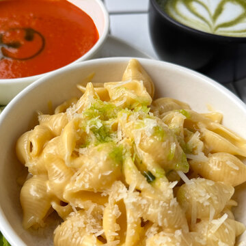 Close-up full frame of creamy cheese Conchiglie pasta shells and a bowl of tomato soup with a matcha latte on a table