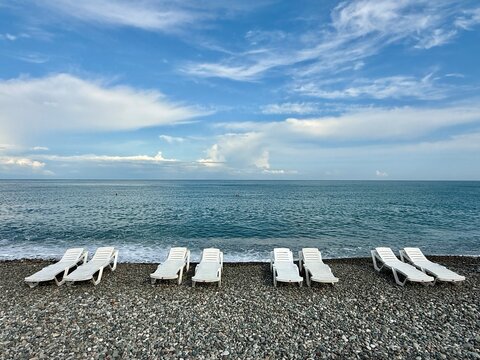 A row of eight empty plastic sun loungers on a pebble beach, Batumi, Adjara, Georgia