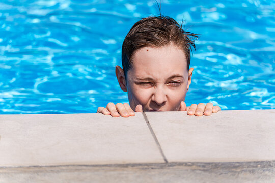 Close-up of a teenage boy squinting and holding the edge of a swimming pool