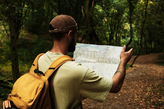 Man with backpack reading a map in Fruska Gora National Park, Serbia. Exploring hiking trail in forest. Rear view - Powered by Adobe