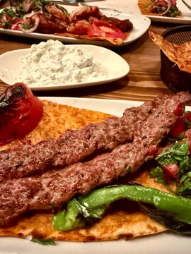 Close-up of a lamb kebab, chicken kebab, yogurt (cacik), pita bread, mixed salad and peppers on a table