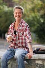 Obraz premium Cheerful tattooed woman holding coffee to go near bag and notebook on street