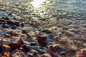 Golden sunset light reflecting on sea waves washing over  and pebbles on the beach shore, relaxing ocean water texture background, natural coastal landscape scene for travel and nature themes.