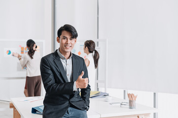 Confident businessman smiling and showing thumbs up to the camera in a modern office, symbolizing success, leadership, and positive achievement.