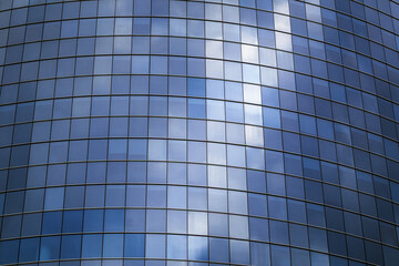 Glass facade of a modern office building with reflective blue windows, showing clouds and sky....