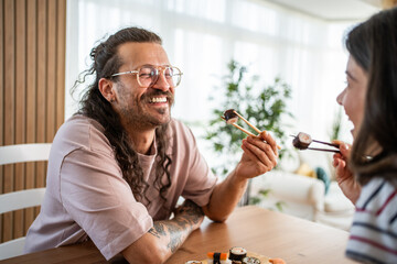 Happy couple sharing sushi rolls with chopsticks at home