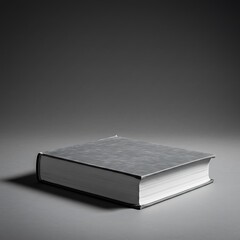 Monochrome still life of a thick, closed hardcover book with a blank cover on a gray surface.