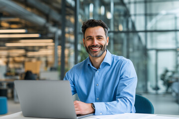 Professional man working on laptop in modern office environment with glass walls during daytime Generative AI