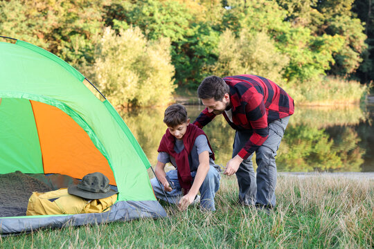 Father and son setting up camping tent near river outdoors - Powered by Adobe