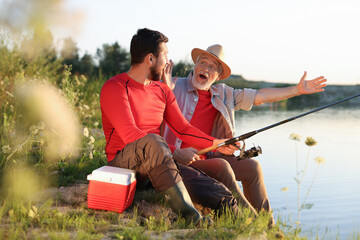 Emotional elderly father and his son fishing together near river outdoors