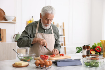 Elderly man cooking at white marble table in kitchen